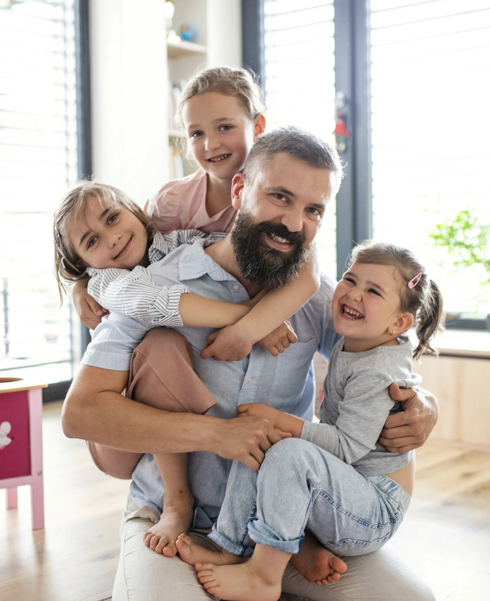 A smiling father hugged by his three young daughters at home